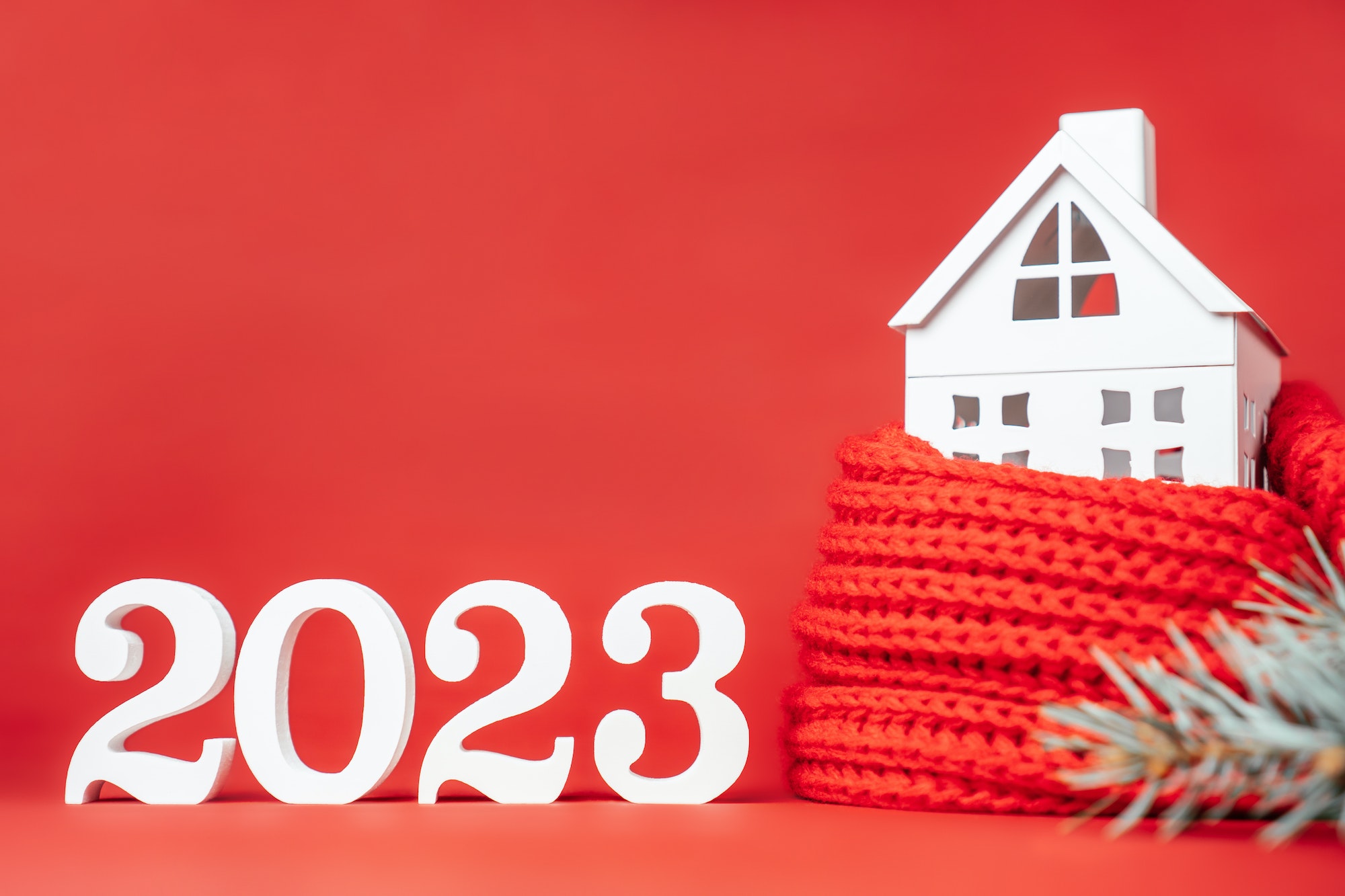White numbers 2023, toy house wrapped in red scarf and spruce branch. Merry Christmas. Copy space